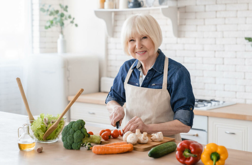 An older adult smiling while chopping vegetables to make a healthy, nutritious meal to reduce bruising.