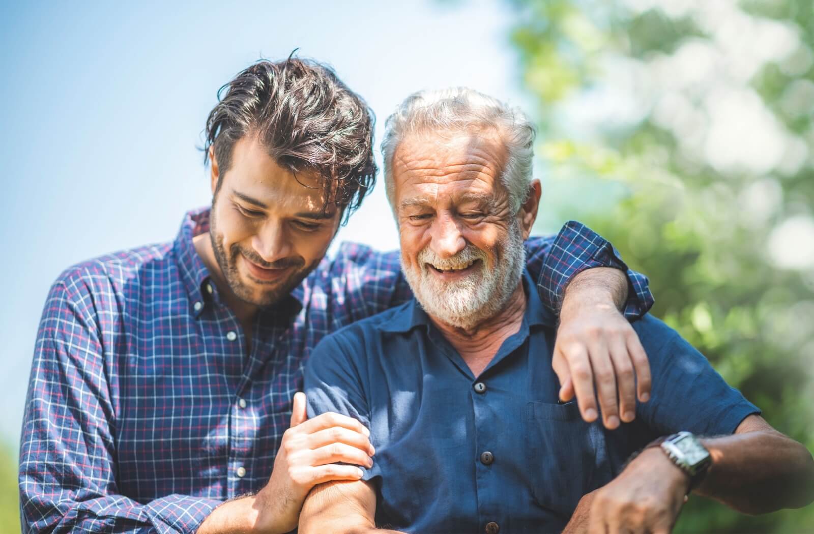An older adult is embraced by their child while sitting outside.