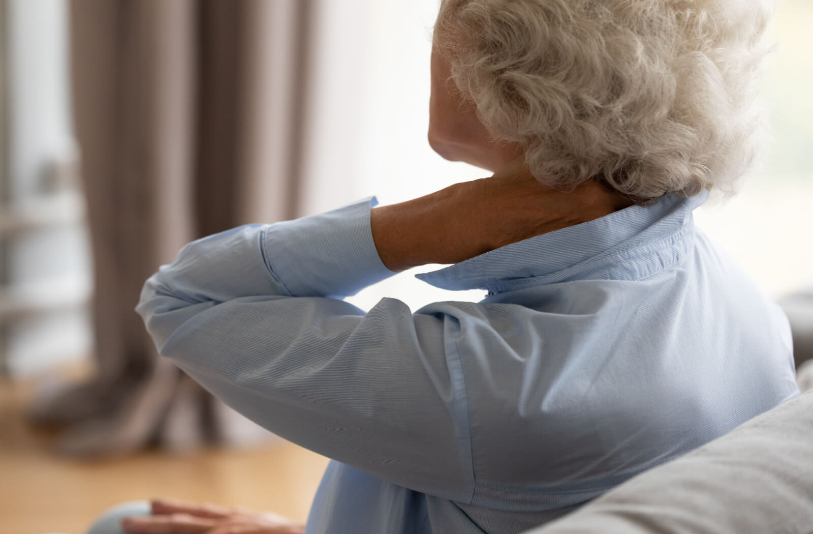 An older adult sitting on the couch and rubbing their neck in discomfort due to a bruise.