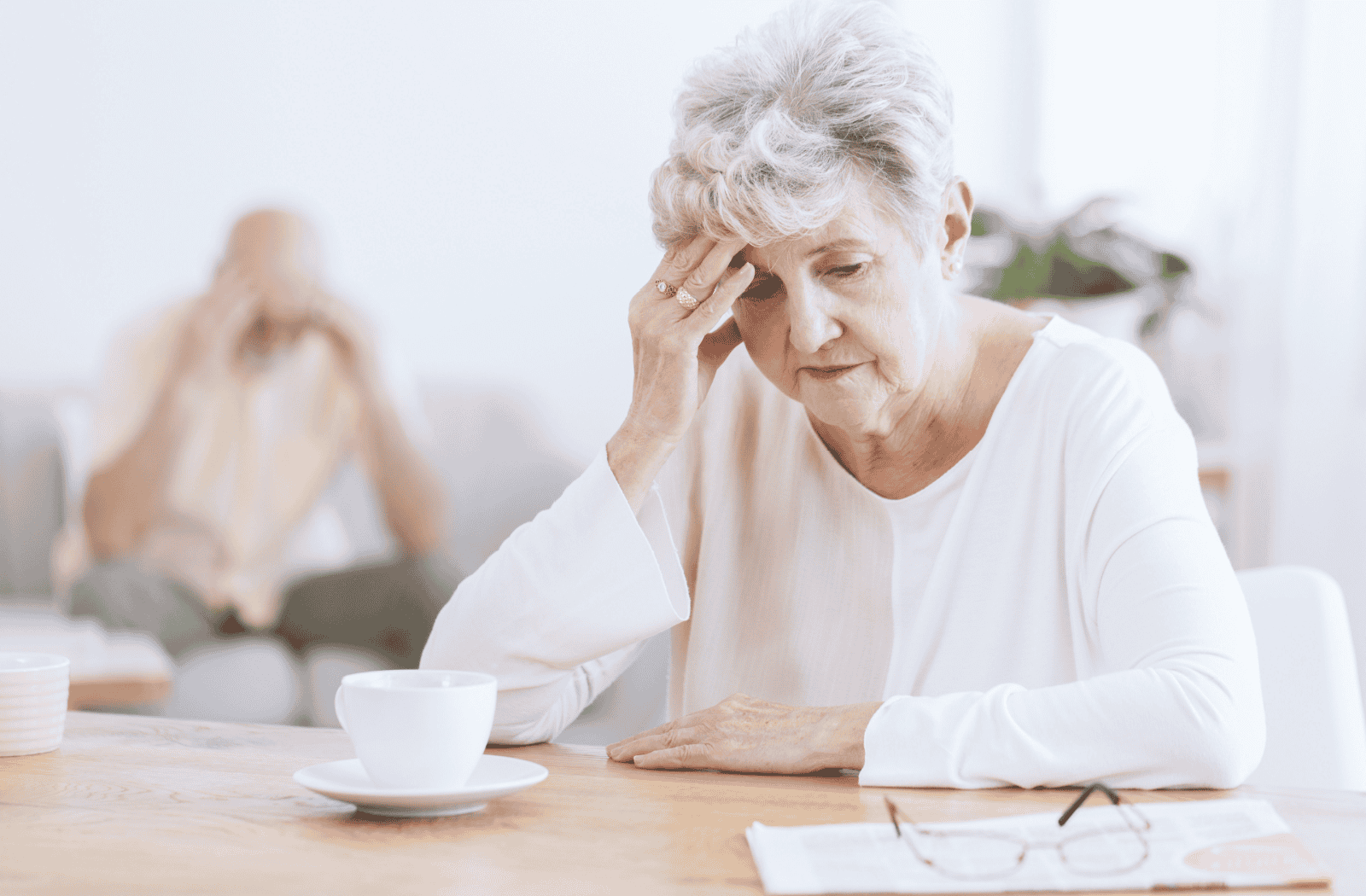 A senior presses their fingers to their temple, staring blankly at a paper on the table.