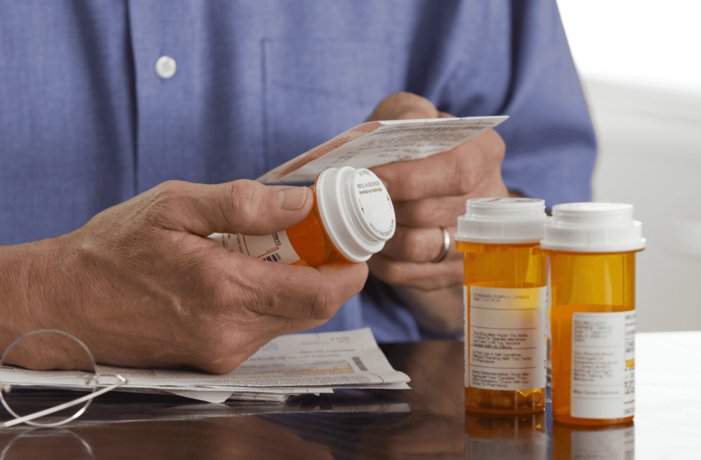 A senior holds a medication bottle, sorting through 3 bottles to find the correct medication.