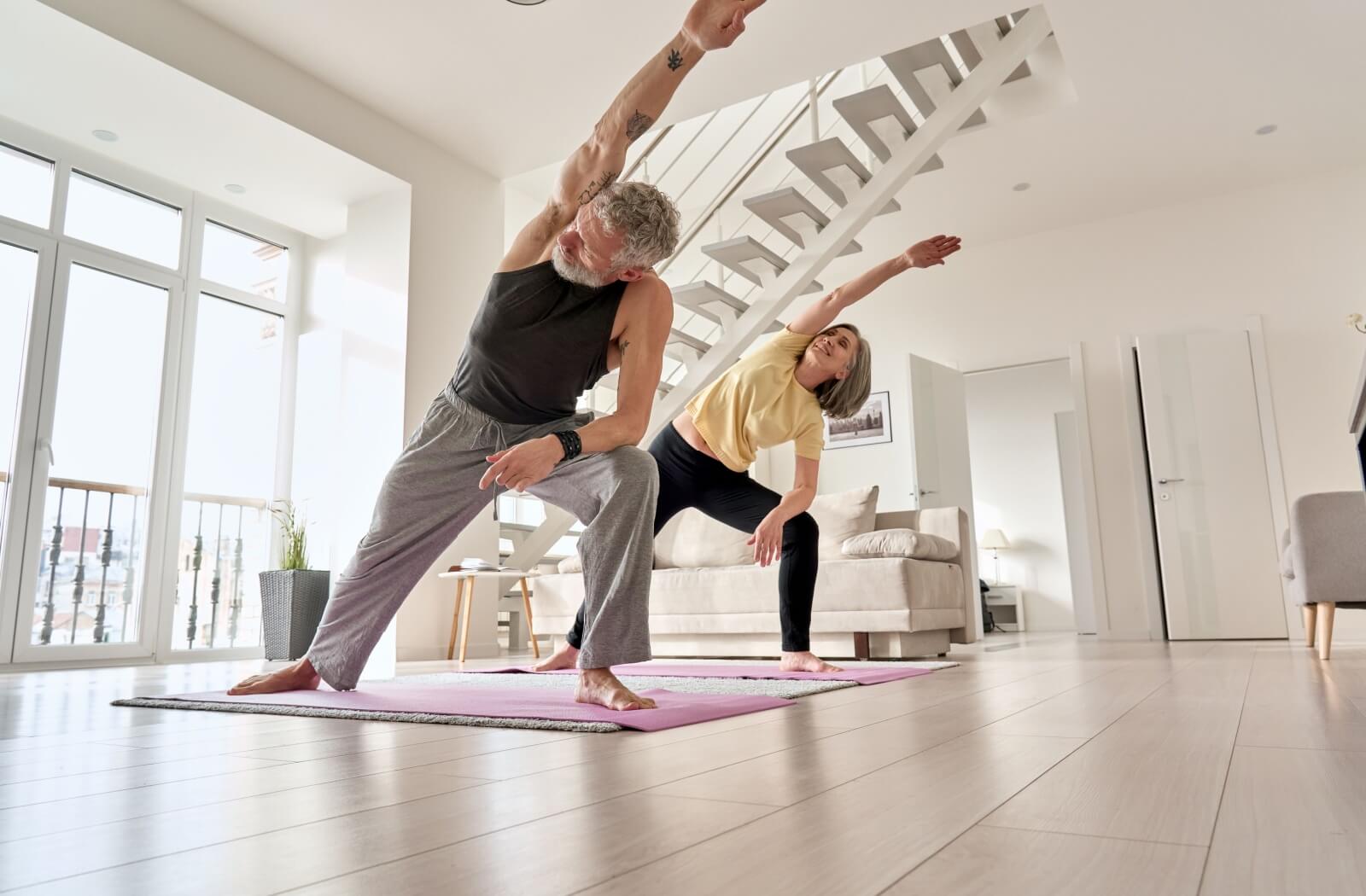 A mature couple practices yoga to strengthen and release their hips.