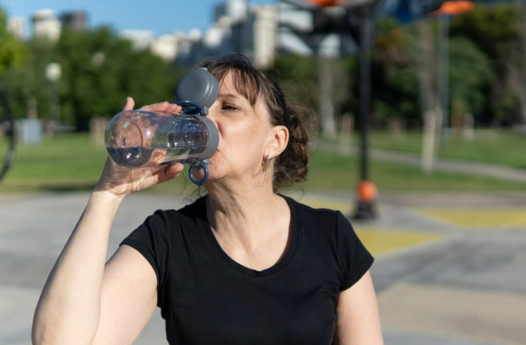An older adult drinking from a reusable water bottle outdoors on a sunny day to stay hydrated during warm-weather activities.