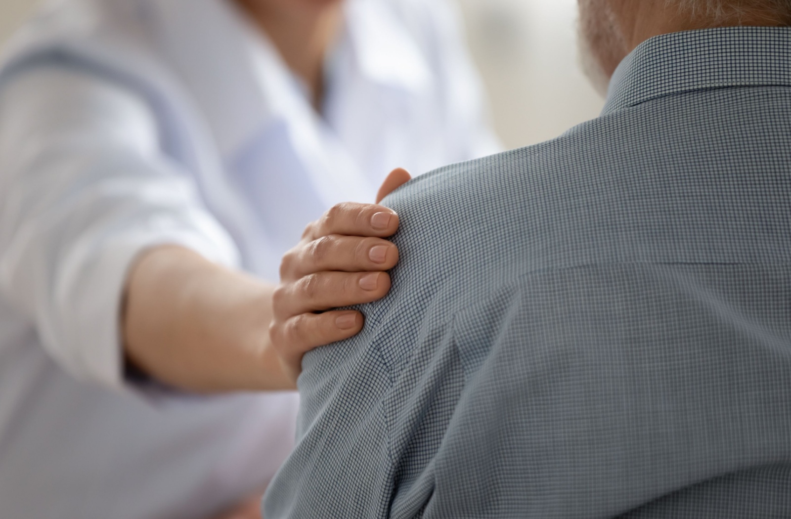 A close-up of a caring adult touching their senior parent's shoulder, expressing empathy and support, while discussing the possibility of dementia.
