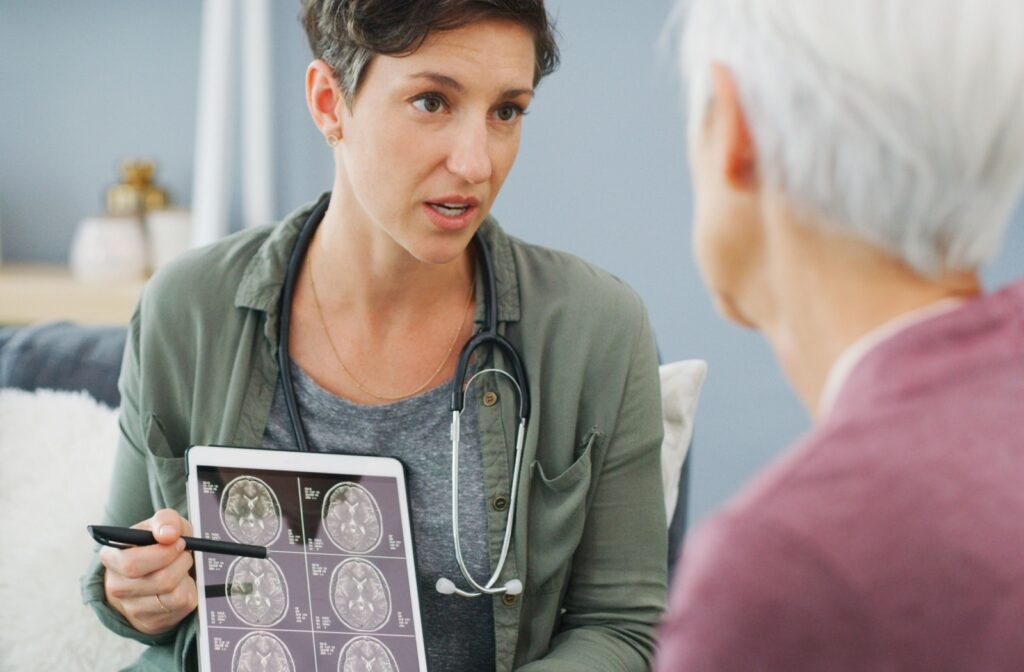 A healthcare professional points at a brain scan on a tablet, advising their senior patient on the progress and symptoms of dementia.