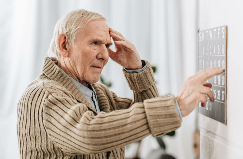 a senior with dementia looks at a calendar while holding his temple