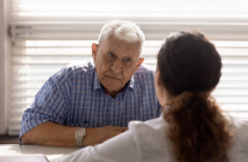 a senior sits at a table listening to a carer