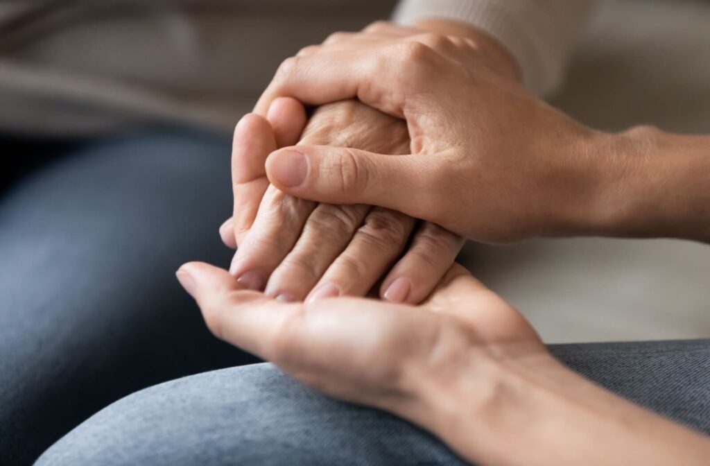 A loved one holds their older loved one's hand to offer comfort and support.