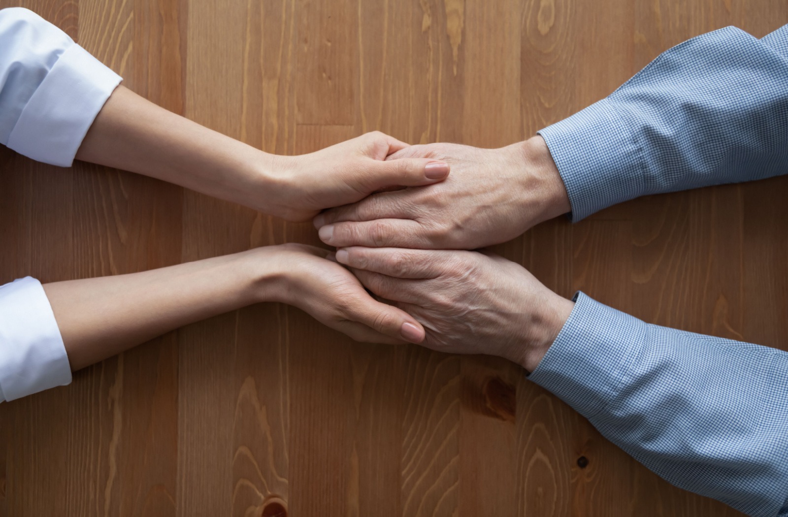 A pair of young adult hands holds an older adult’s hands, offering comfort after a dementia diagnosis.